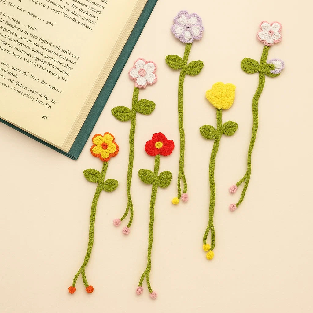 Eight crocheted flower bookmarks from the Crochet Flower Bookmark Kit are displayed on a light surface beside an open book—charming handmade gifts for book lovers.