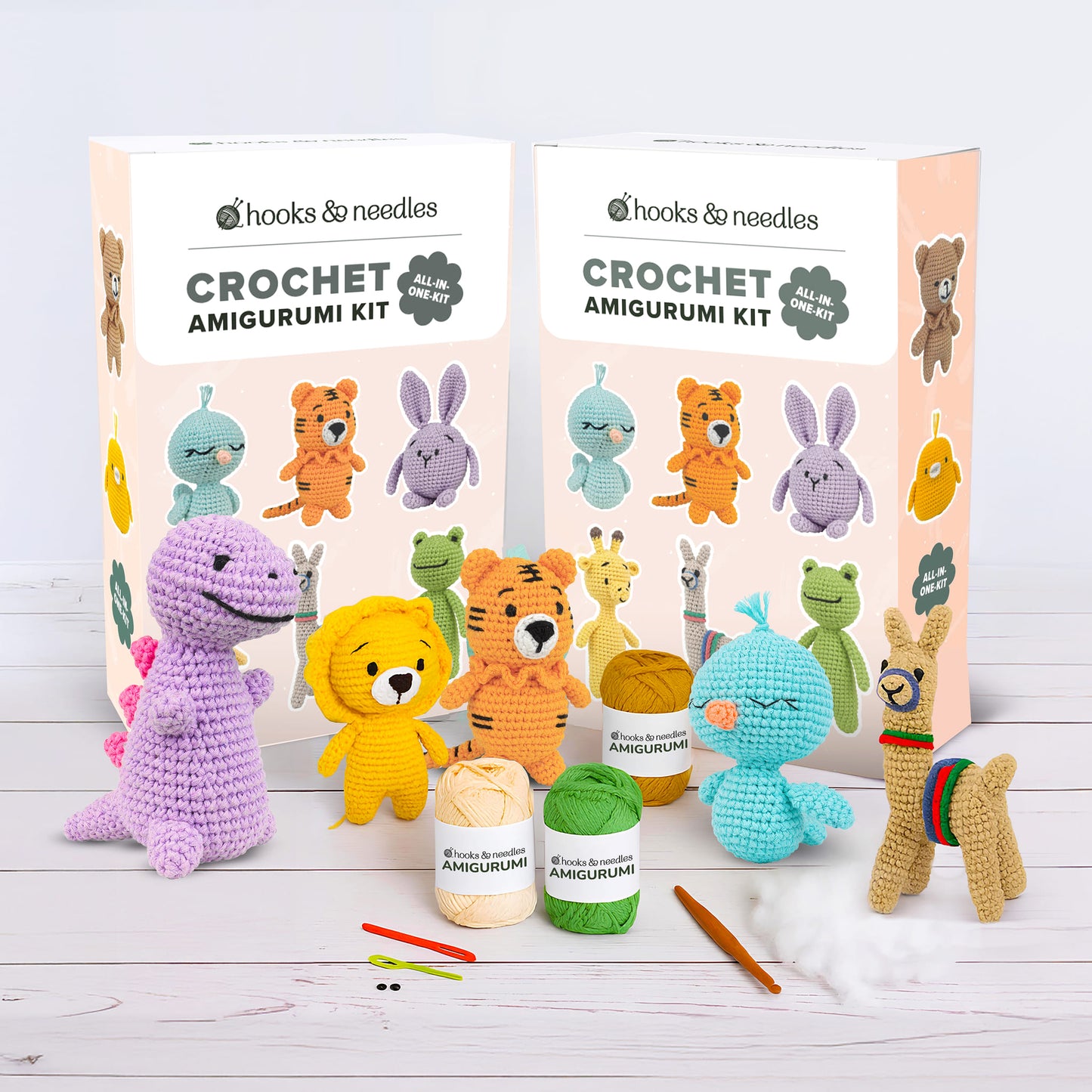 The Amigurumi Subscription Box 2 features two animal-themed crochet kits, complete with yarn, hooks, and stuffing, displayed alongside finished crochet animals on a white wooden surface.