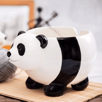 The Panda Ceramic Yarn Bowl sits on a bamboo mat with a gray yarn ball nearby—ideal for beginner-friendly projects like cozy blankets—against a blurred background.