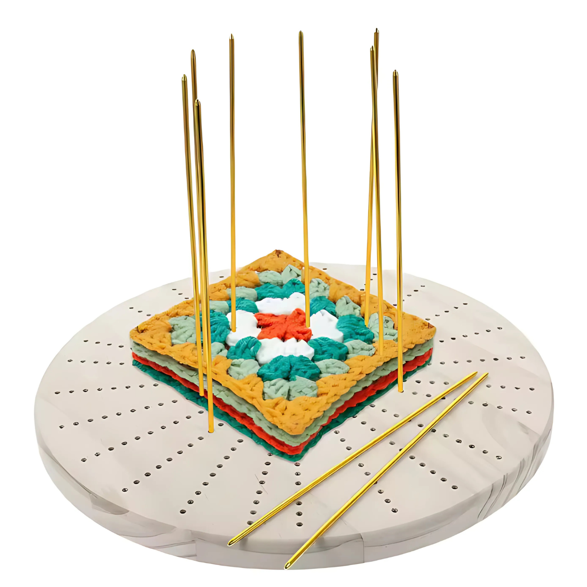 A Round Crochet Blocking Board features a centered crocheted granny square on its circular grid, with golden premium steel pins inserted vertically and two pins resting on the surface.