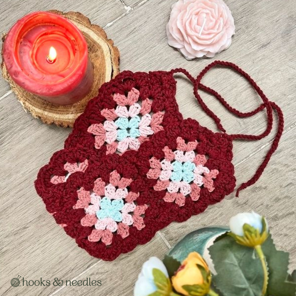 Vintage Headband Crochet Pattern featuring red, pink, and white granny squares, displayed on wood with a red candle, a pink rose, and yellow flowers.
