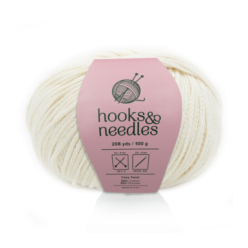A skein of Cozy Twist Yarn in off-white features 208 yards, 100 grams, and a blend of 85% cotton and 15% acrylic on a pink "hooks & needles" band—ideal for soft, durable, and versatile projects.