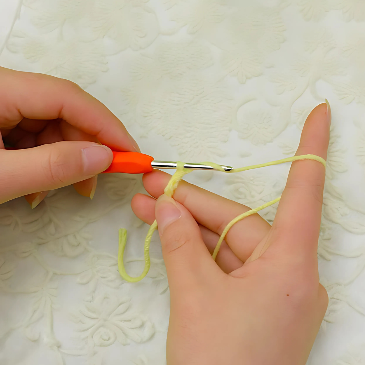Hands holding an orange-handled crochet hook and yellow yarn, ready to start a crochet home decor project using the Crochet Cactus Kit 3pcs on a textured white surface.