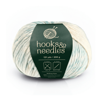Shifting Hues: A 200g skein of bulky cream and pale blue yarn (131 yds), made from 100% mulesing-free wool with a green "hooks & needles" label—ideal for projects needing luxurious warmth.