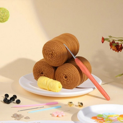 Three brown yarn skeins, a crochet hook, yellow thread, beads, and more—everything you need in the Crochet Poodle Kit to assemble your own poodle or start a fun beginner crochet project.