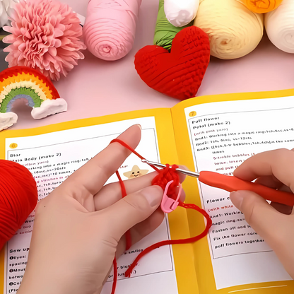 Crocheting with red yarn and a hook, guided by an open pattern book, and surrounded by colorful yarn—ideal for beginners using the Crochet Keychain Kit 4pcs to make handmade keychains.