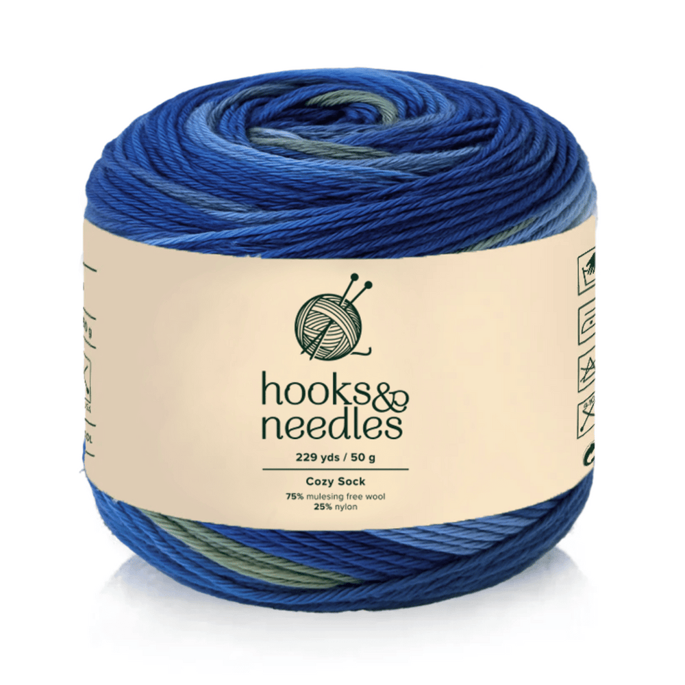 A 50g skein of Cozy Sock blue gradient yarn, 229 yds, 75% mulesing-free wool/25% nylon for cozy warmth and durability; knitting and care symbols are visible on the label.