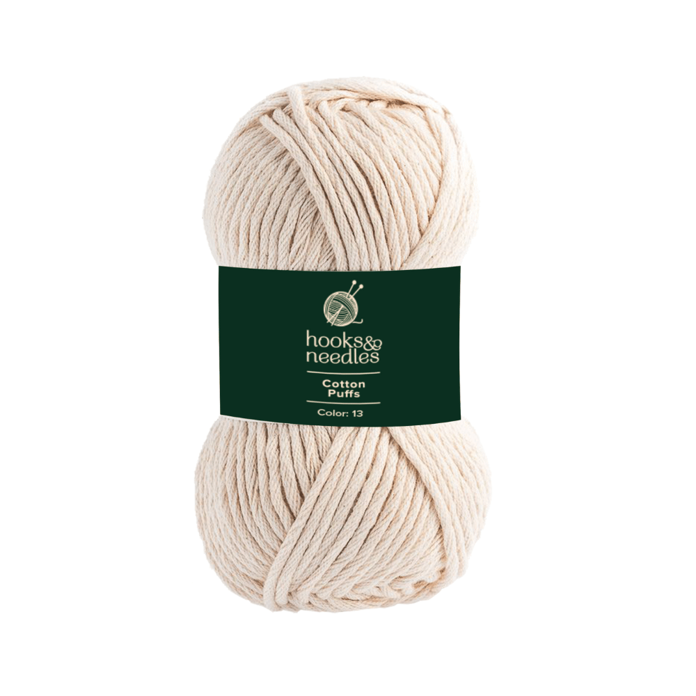 A skein of cotton yarn in a cream color and chunky texture, with a dark green label that reads "hooks & needles, Cotton Puffs Yarn 100g, Color 13.