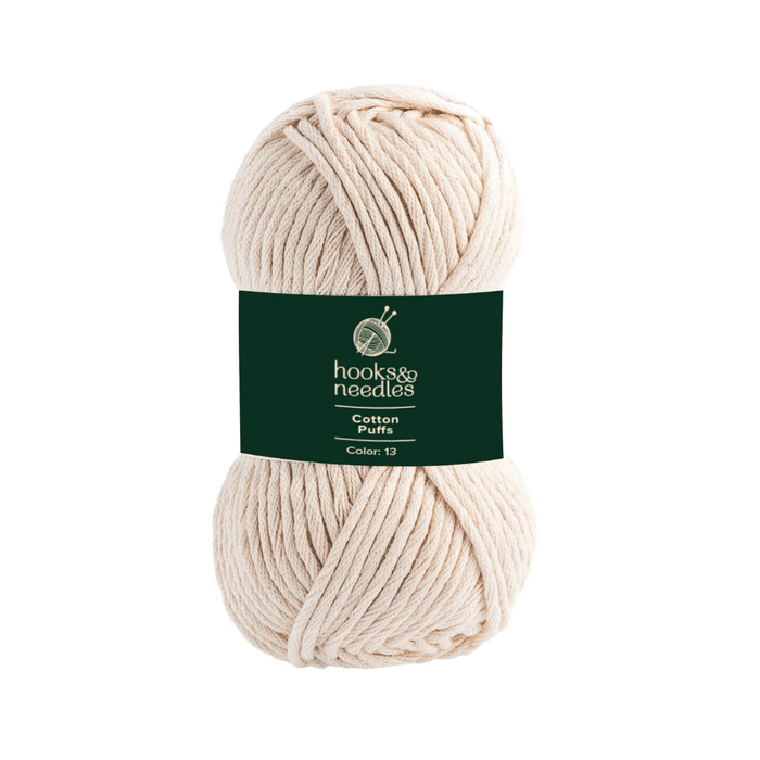 A skein of cotton yarn in a cream color and chunky texture, with a dark green label that reads "hooks & needles, Cotton Puffs Yarn 100g, Color 13.