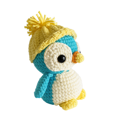 Frosty The Penguin is a crocheted blue and white plush toy wearing a yellow knit pom-pom hat, made from an intermediate crochet pattern and displayed on a plain white background.