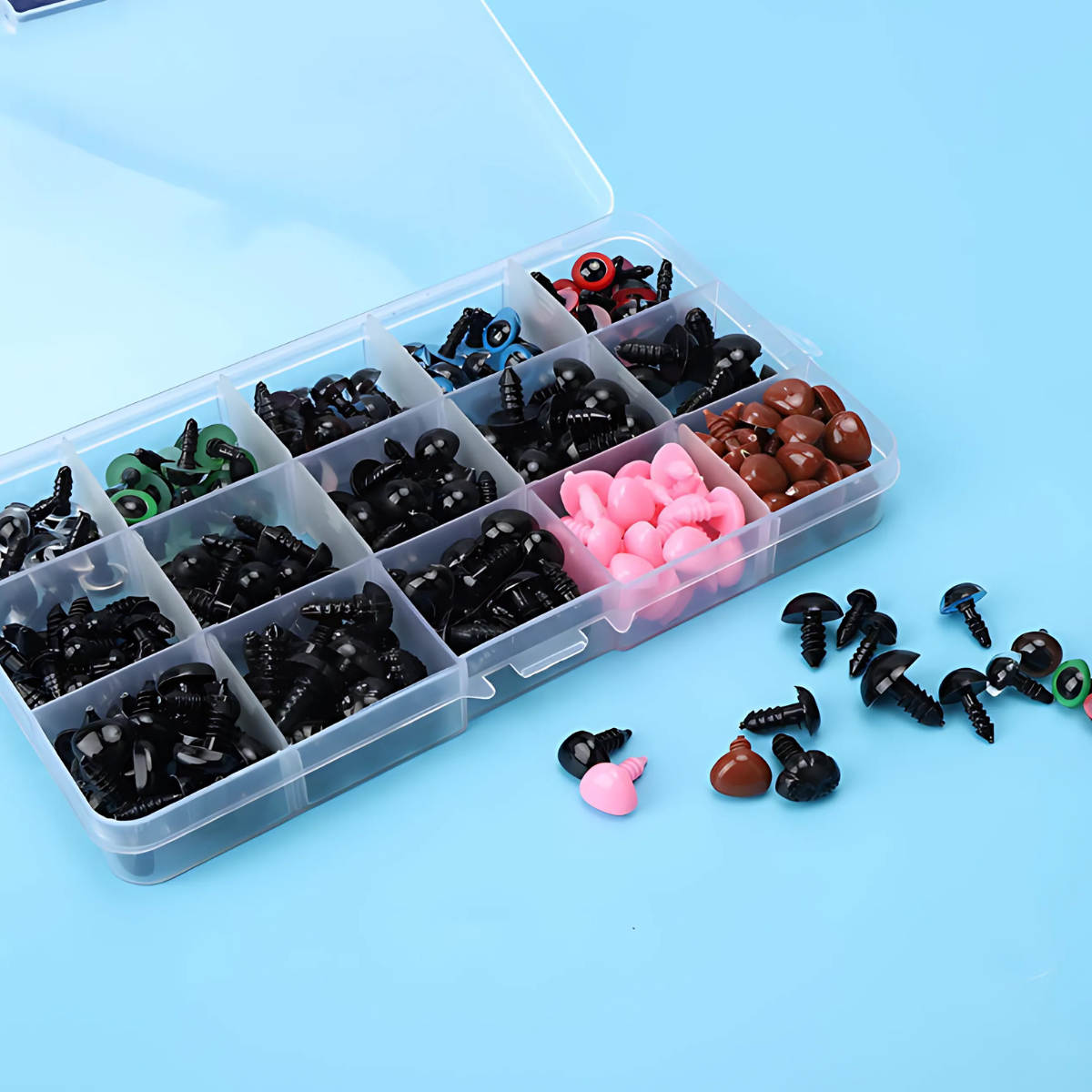 The Crafting Safety Eyes & Noses Set includes assorted colorful eyes and noses in various sizes, neatly organized in a plastic storage box with compartments. Some pieces are displayed outside the box on a blue surface.