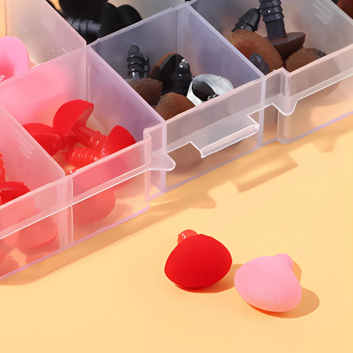 A plastic organizer box with compartments holds Safety Noses for Toys with Washers in red, pink, black, brown, and white—ideal for customizing crochet toys or amigurumi. Two noses are placed outside the box.
