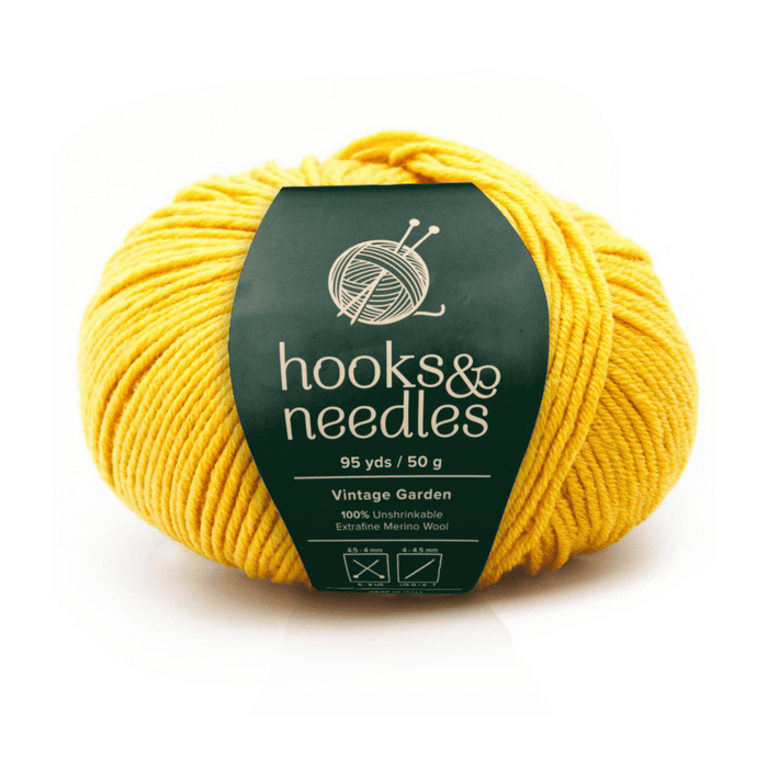 A 50g, 95yd ball of yellow "Vintage Garden" yarn (100% extra-fine merino wool) labeled "hooks & needles" offers luxurious softness with clear washing and ironing care symbols on the label.