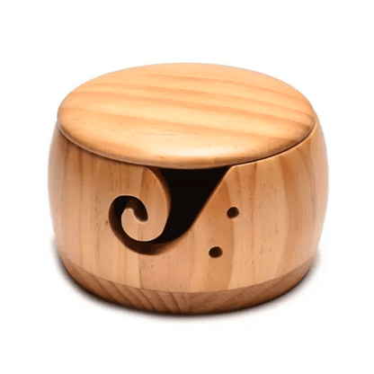 The Wooden Yarn Bowl With Lid is adorned with a decorative cutout swirl and features two small holes on the side, making it ideal for organizing your knitting accessories.