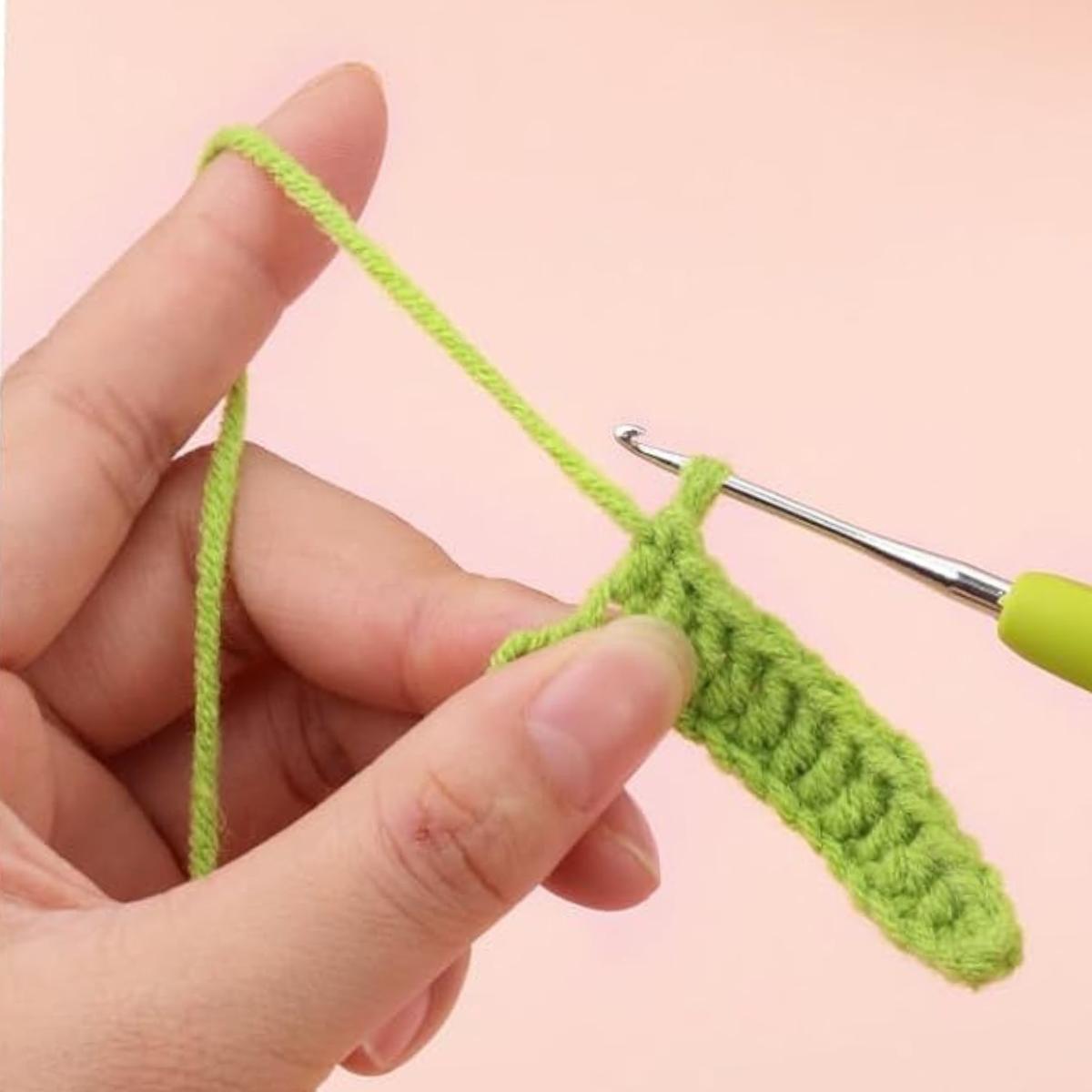 A hand holds green yarn and a crochet hook, working on a piece from the Crochet Tulip Bouquet Kit—ideal for crafting an everlasting tulip arrangement or a heartfelt crochet gift—set against a plain background.