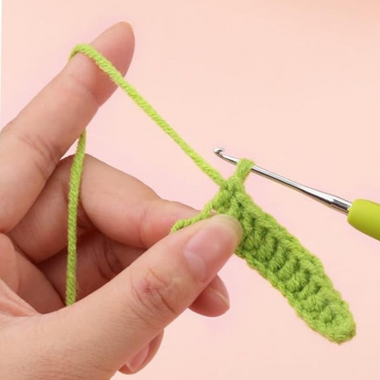 A hand holds green yarn and a crochet hook, working on a piece from the Crochet Tulip Bouquet Kit—ideal for crafting an everlasting tulip arrangement or a heartfelt crochet gift—set against a plain background.