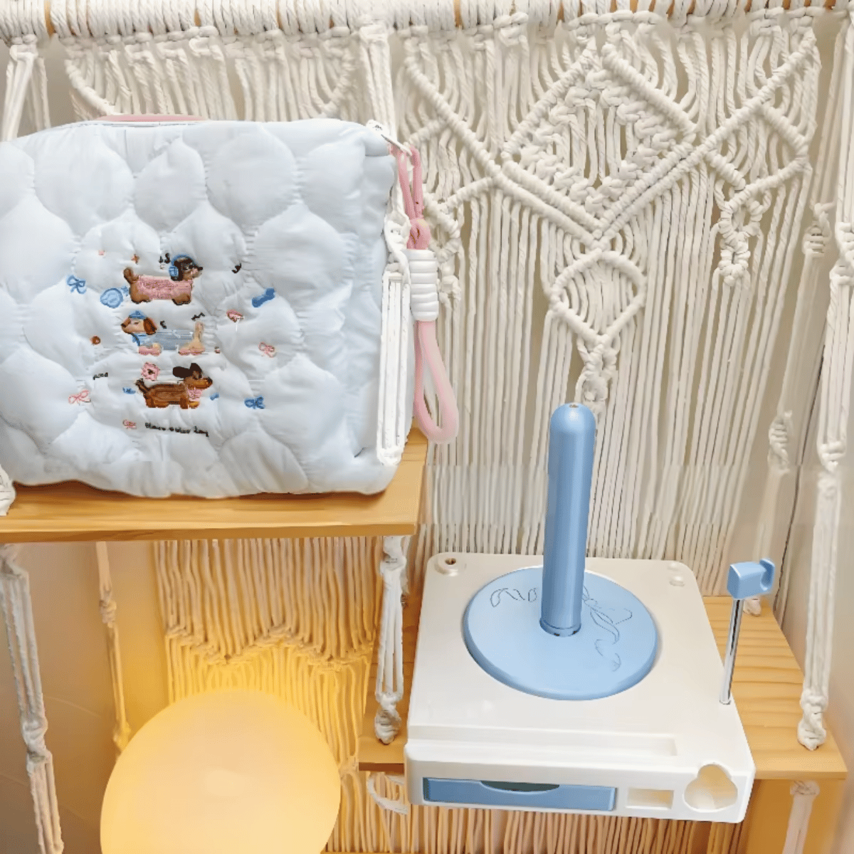 The Spinning Yarn Holder with Tool Storage, featuring animal designs and a quilted pouch, sits by a blue and white toilet training toy against a macrame backdrop—perfect for organizing crafting essentials.