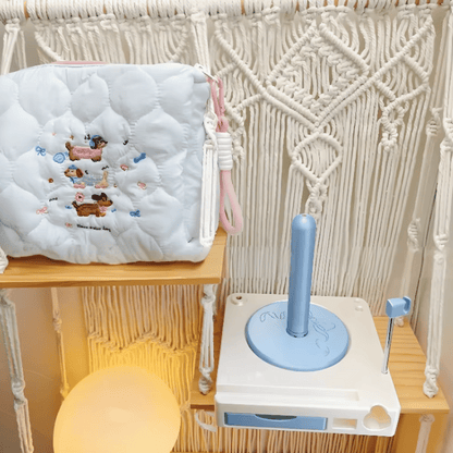 The Spinning Yarn Holder with Tool Storage, featuring animal designs and a quilted pouch, sits by a blue and white toilet training toy against a macrame backdrop—perfect for organizing crafting essentials.