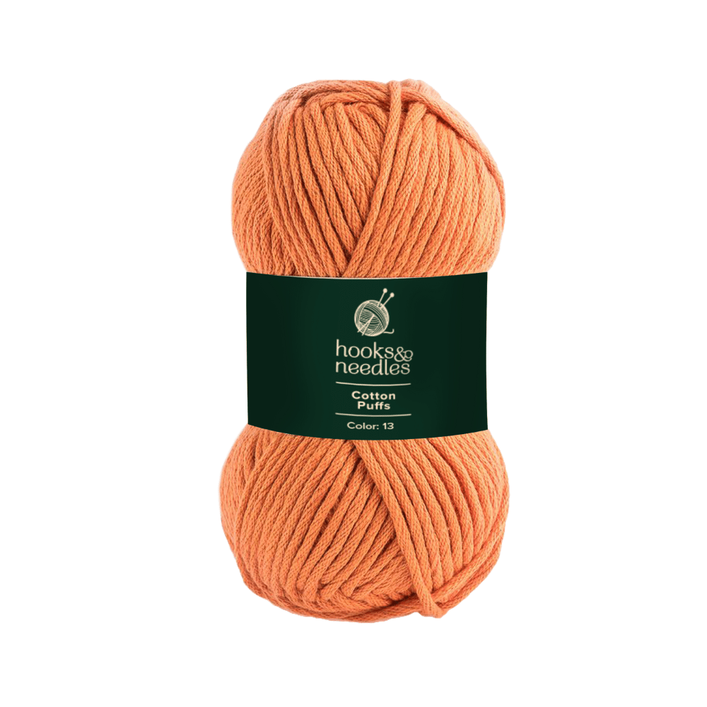 A skein of orange chunky texture yarn with a dark green label that reads "hooks & needles, Cotton Puffs Yarn 100g, Color: 13.