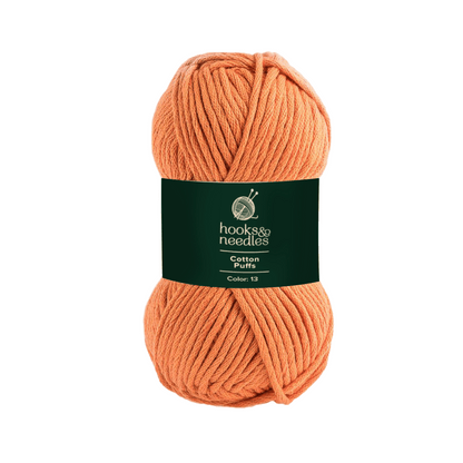 A skein of orange chunky texture yarn with a dark green label that reads "hooks & needles, Cotton Puffs Yarn 100g, Color: 13.