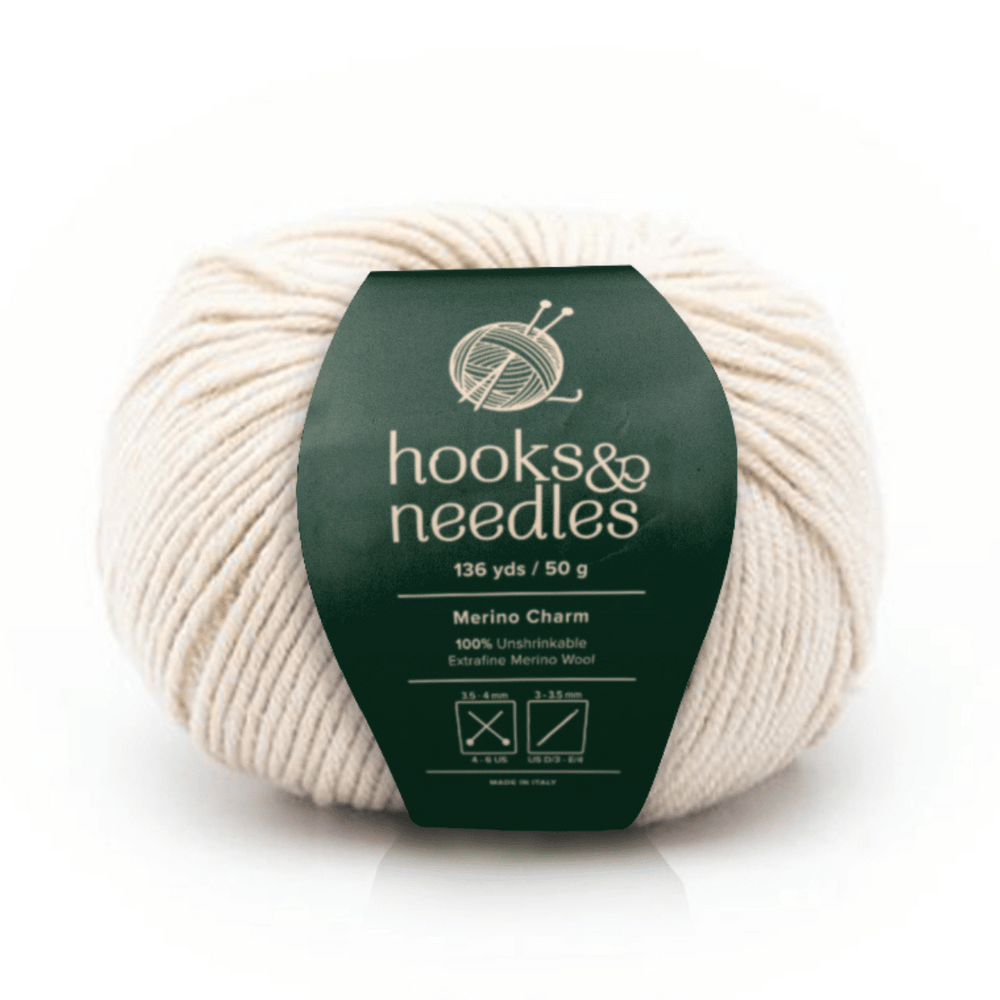 Merino Charm Yarn 50g is a cream-colored, unshrinkable yarn made of 100% Extrafine Merino Wool (136 yds per 50g), featuring a green "hooks & needles" label. Ideal for soft, durable projects.