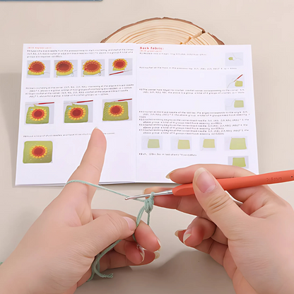 Using a Crochet Bag Kit, someone crafts a sunflower bag from green yarn with a crochet hook, following illustrated step-by-step instructions in an open pattern booklet on the tabletop.