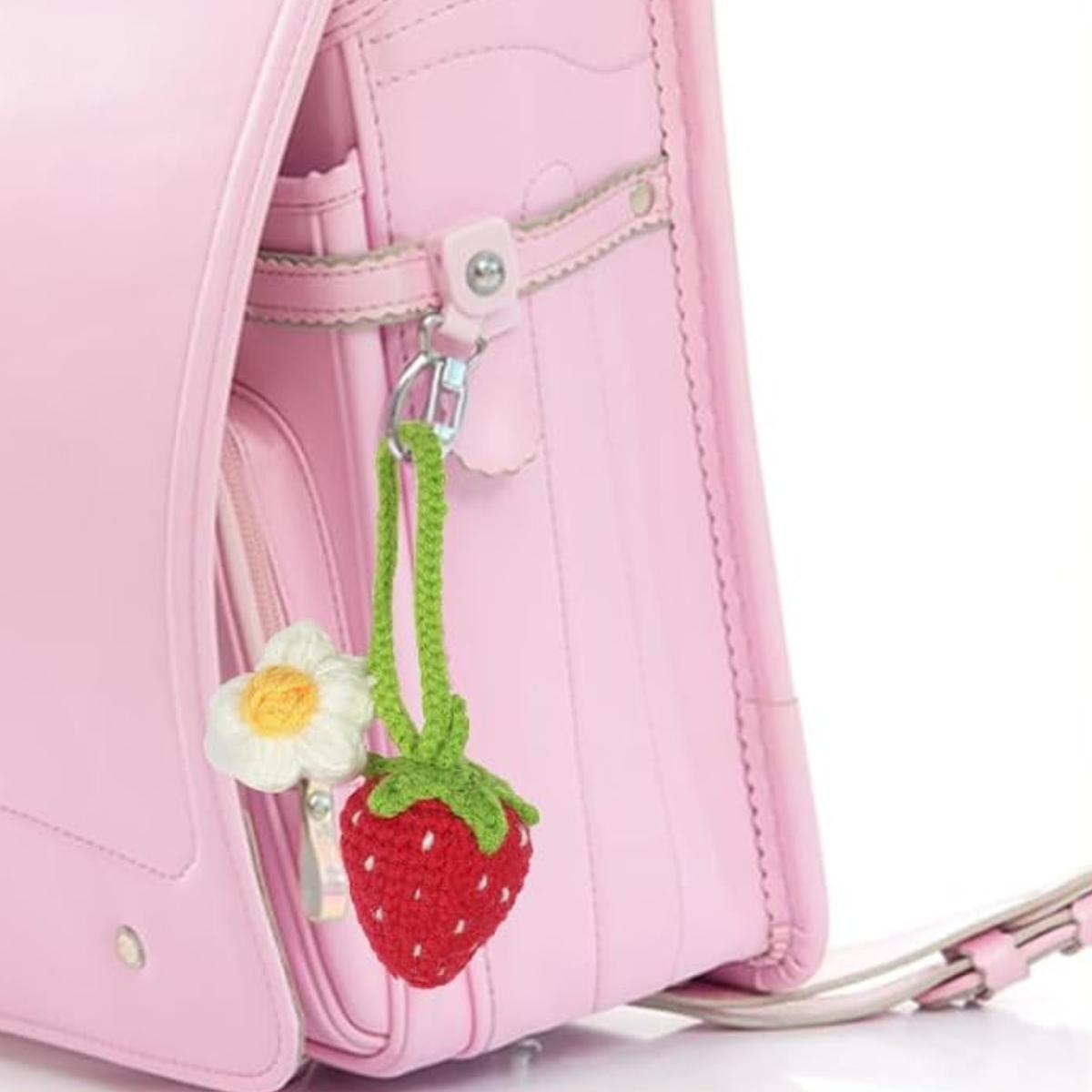 A pink leather backpack with a crocheted strawberry and flower keychain from the Crochet Fruits Kit 4pcs, attached to the side pocket.
