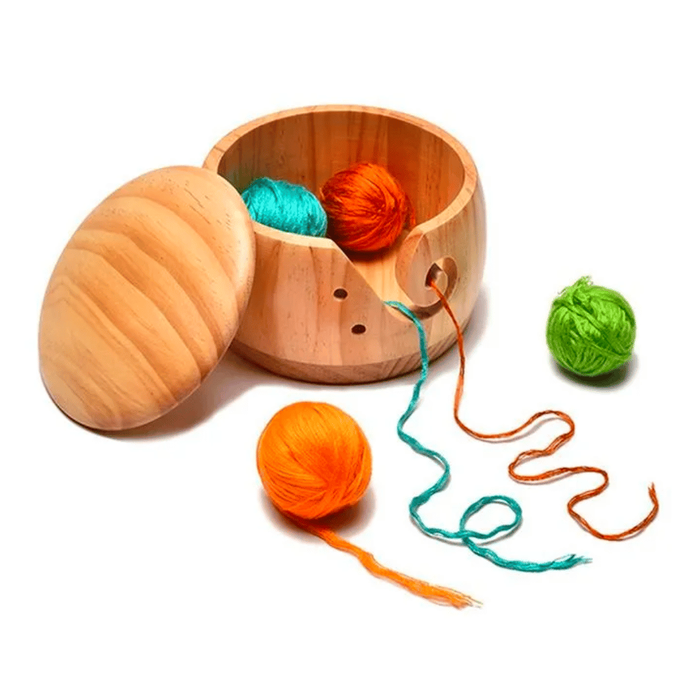 The Wooden Yarn Bowl With Lid is designed to hold three balls of yarn—orange, green, and teal. It serves as an ideal knitting accessory with one orange and one teal strand extending outward.