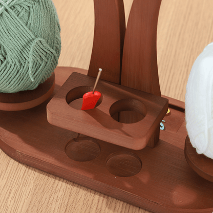 The Double Yarn Spinner Stand with Tool Storage keeps green and white yarn balls tangle-free, features a red-heart-topped pin, and sits on a light wood surface—perfect for organized, stylish crafting and efficient yarn storage.