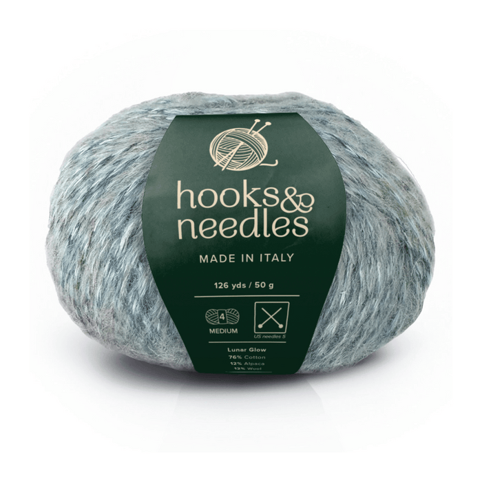 A 50g, 126 yd ball of Lunar Glow yarn, gray and bulky weight, labeled "hooks & needles, Made in Italy." The green wrapper details mulesing-free wool fiber content and care instructions.