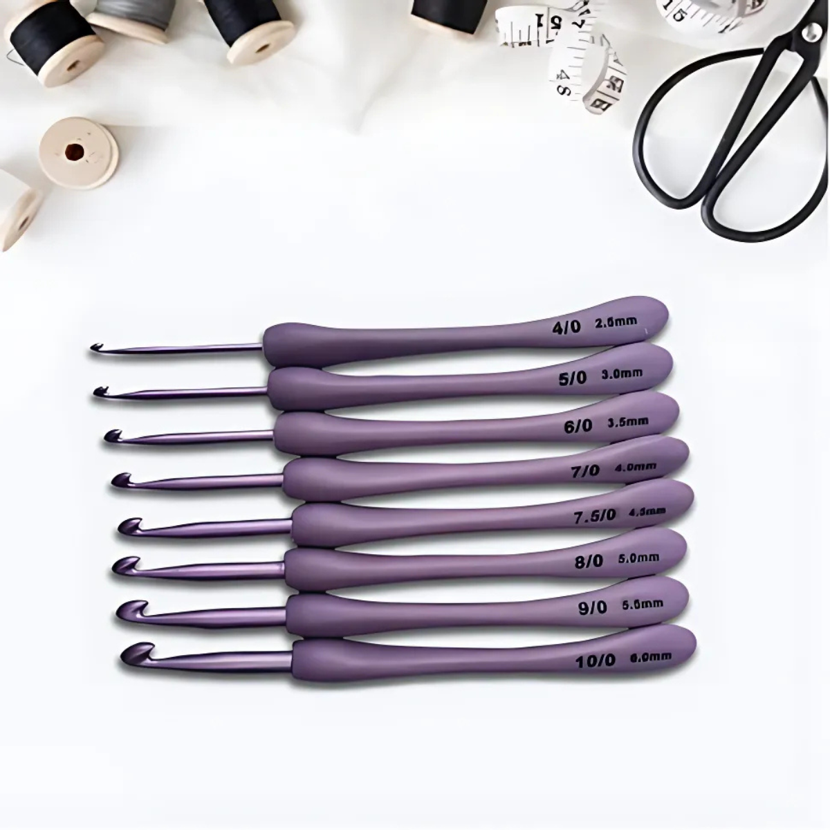 The 8 Pcs Purple Crochet Hook Set, featuring ergonomic hooks in assorted sizes, is displayed on a white surface alongside sewing thread spools, a tape measure, and scissors.
