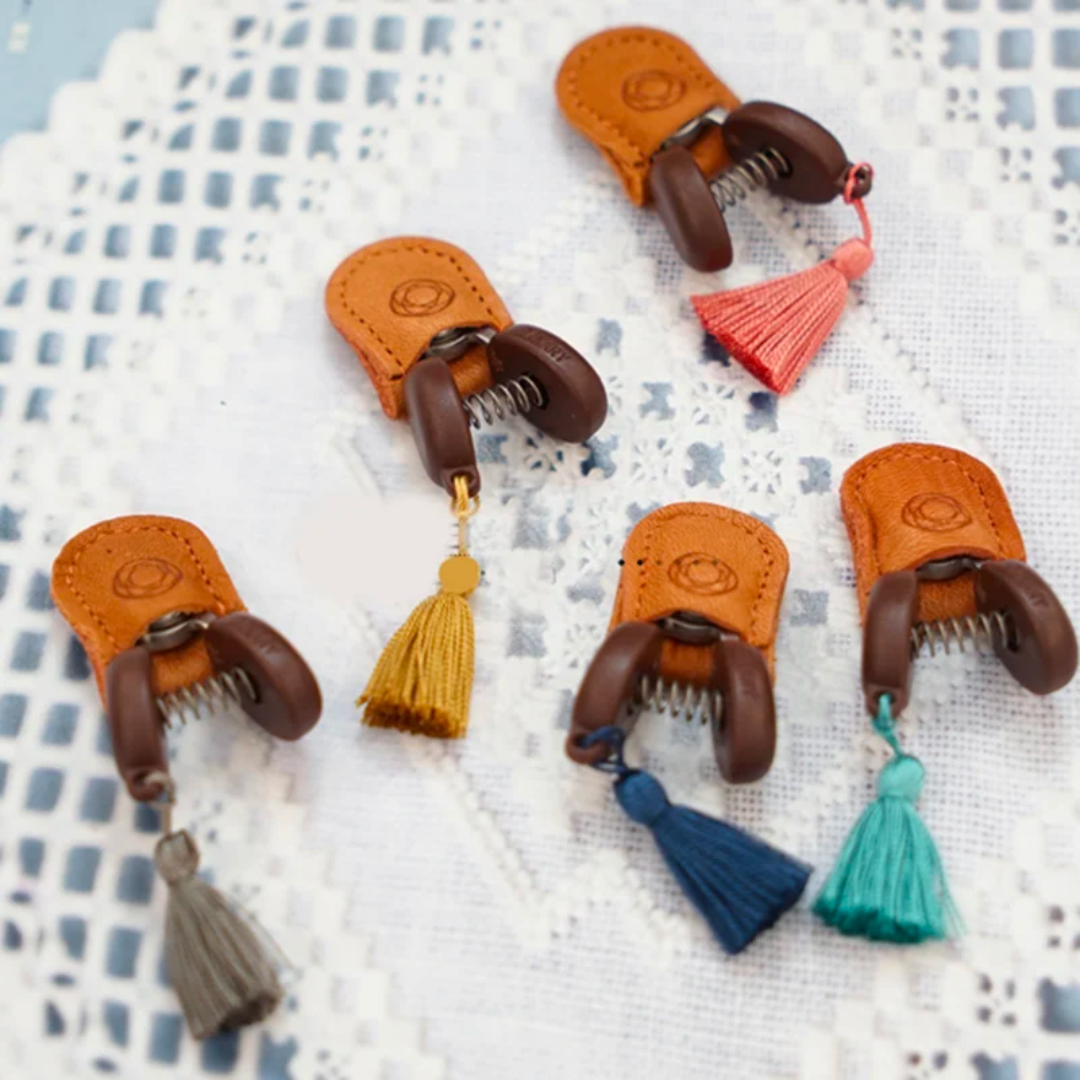 Five pairs of precision-crafted Small Scissors featuring leather and wood tassel accents in various colors rest elegantly on a lace background, showcasing their compact and portable design, perfect for any accessory collection.