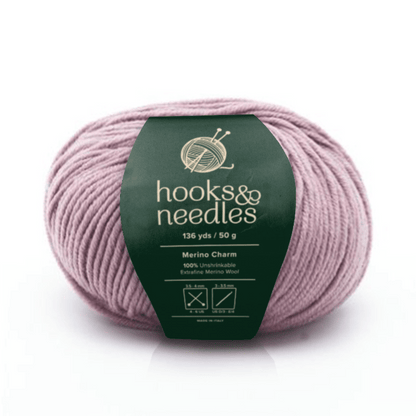 A ball of light mauve Merino Charm Yarn 50g with care instructions and logo on a green "hooks & needles" wrapper.