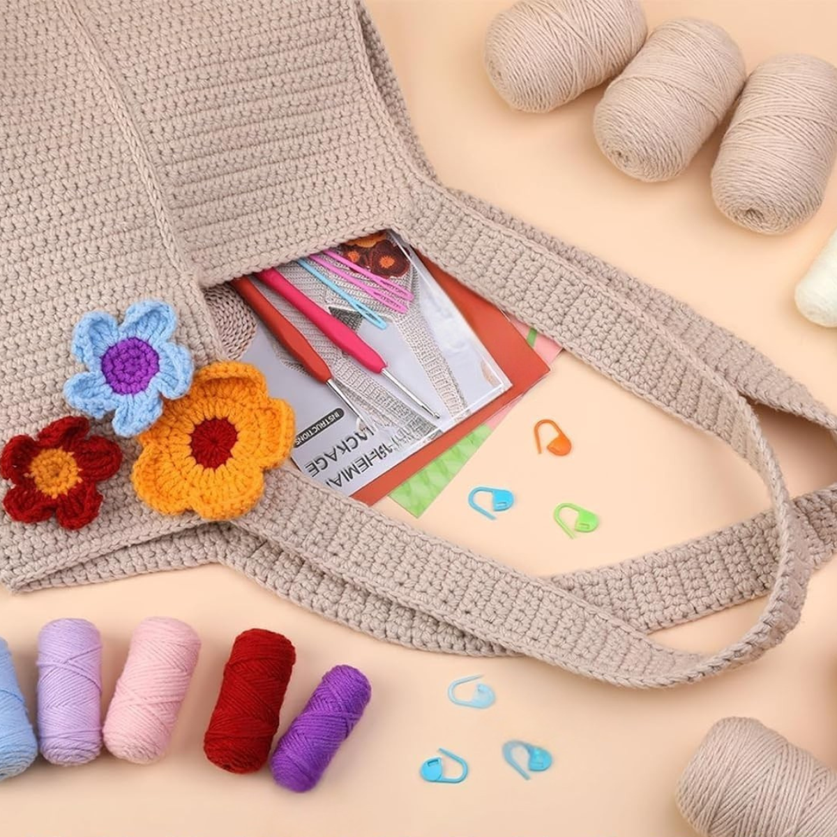 The Bohemian Crochet Tote Bag Kit features a beige cotton yarn bag embellished with vibrant crocheted flowers, plus yarn balls, hooks, stitch markers, and space for notebooks and pens—combining charm and practicality.