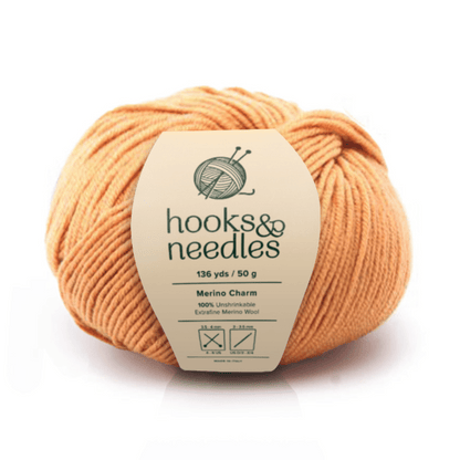 A skein of Merino Charm Yarn 50g in orange (136 yds, 100% extrafine merino wool) features washing, ironing, and drying icons—an unshrinkable yarn combining softness with durability.