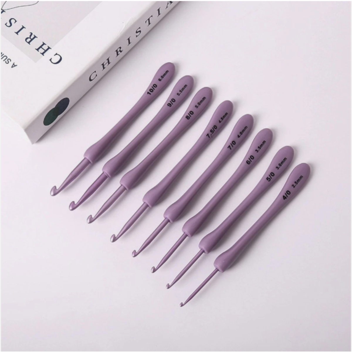 Eight purple ergonomic crochet hooks from the 8 Pcs Purple Crochet Hook Set are arranged in a row next to a partially visible white box. Each comfortable hook is labeled with its size in millimeters.