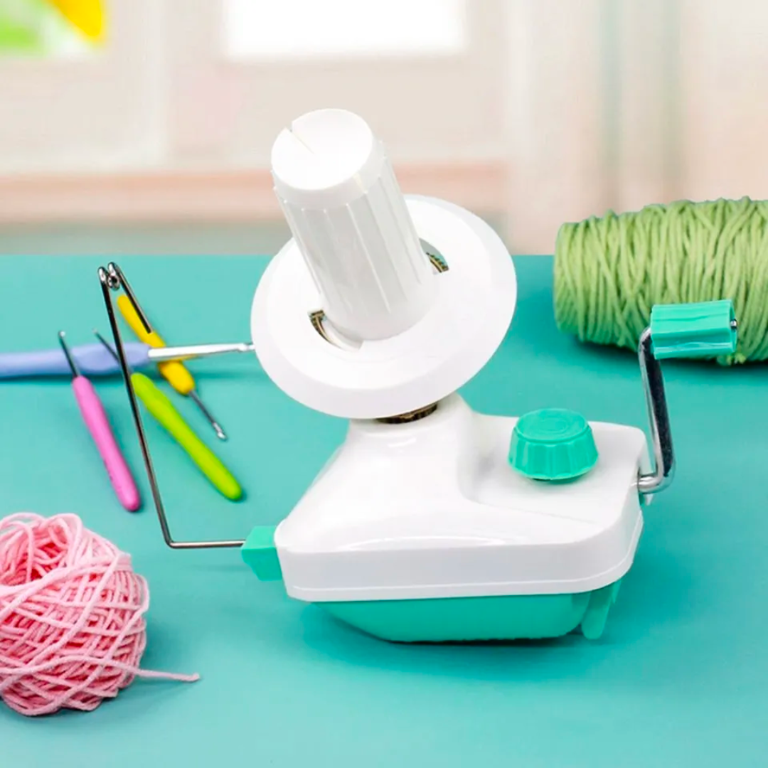 A small white Yarn Ball Winder on a teal surface with crochet hooks and balls of yarn.