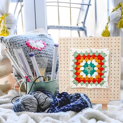 A cozy crochet corner with yarn balls, crochet hooks, and a granny square on a Crochet Blocking Board display stand.