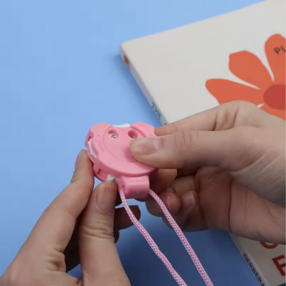 A person holds a pink Row Counter for Knitting & Crocheting with a lanyard, perfect as a crochet accessory, in front of a book featuring an orange flower on the cover.