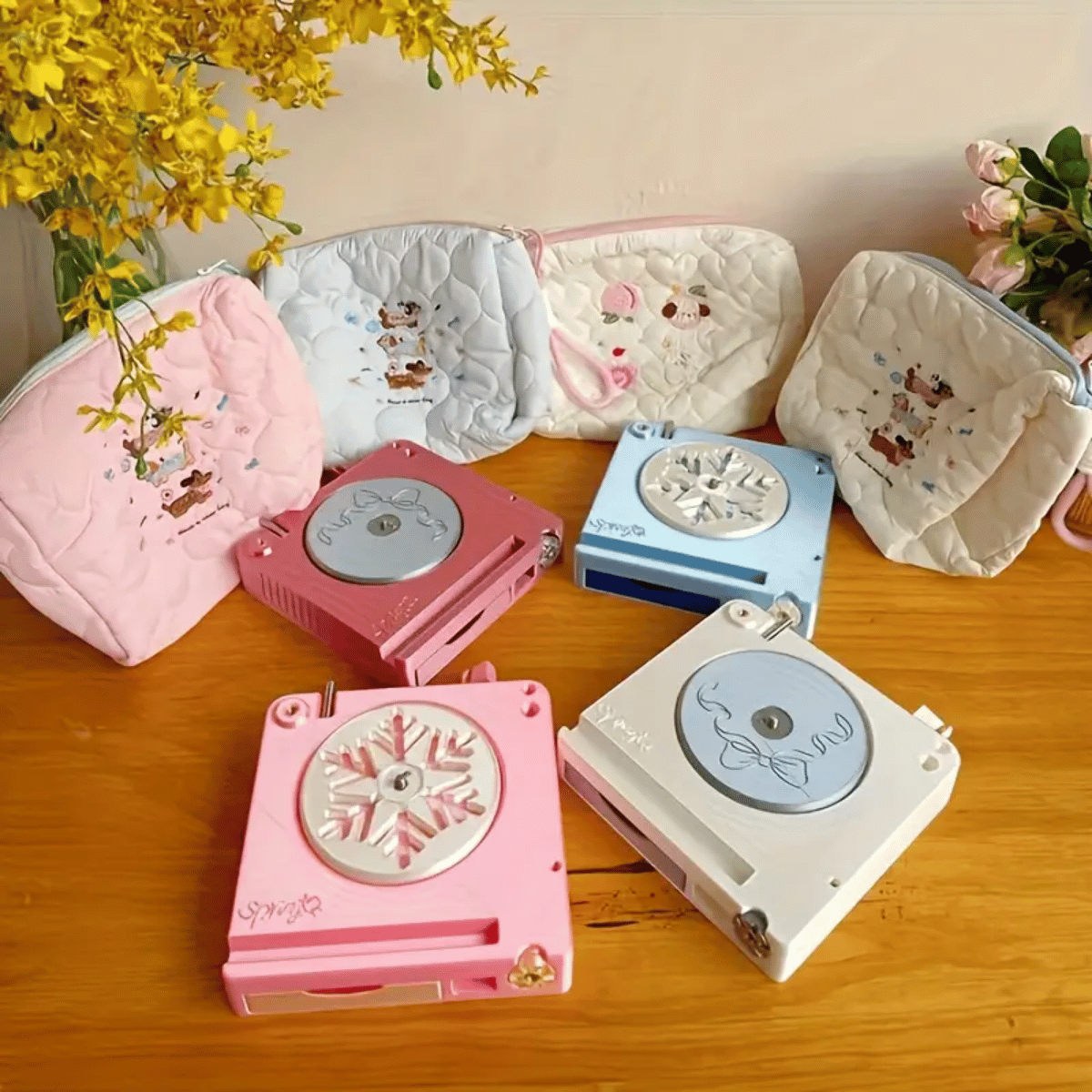 Three quilted pouches with animal designs and four portable mini music boxes in pink, blue, and white sit on a wooden table with flowers, offering charming storage for your Spinning Yarn Holder with Tool Storage or creative essentials.
