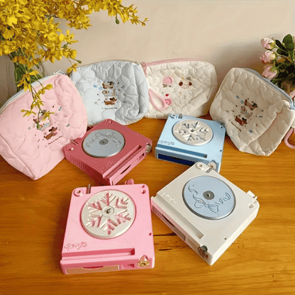 Three quilted pouches with animal designs and four portable mini music boxes in pink, blue, and white sit on a wooden table with flowers, offering charming storage for your Spinning Yarn Holder with Tool Storage or creative essentials.