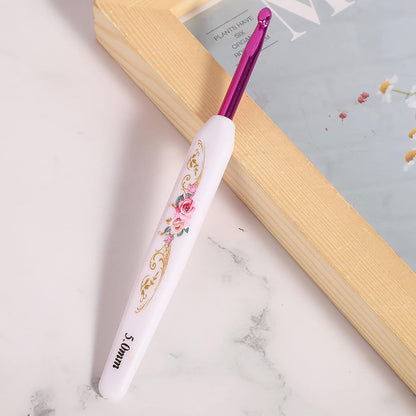 A "Crochet Hook Set 16 Pcs with Case" features a lightweight crochet hook with a white handle, pink floral designs, and metallic pink 5.0mm tip, resting on marble near a wooden frame—blending artistry and function.