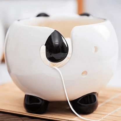 The Panda Ceramic Yarn Bowl—round and panda-shaped with black ears, feet, and tail—holds a white spoon in its side slot, making it a charming way to serve snacks during beginner-friendly knitting loom sessions.