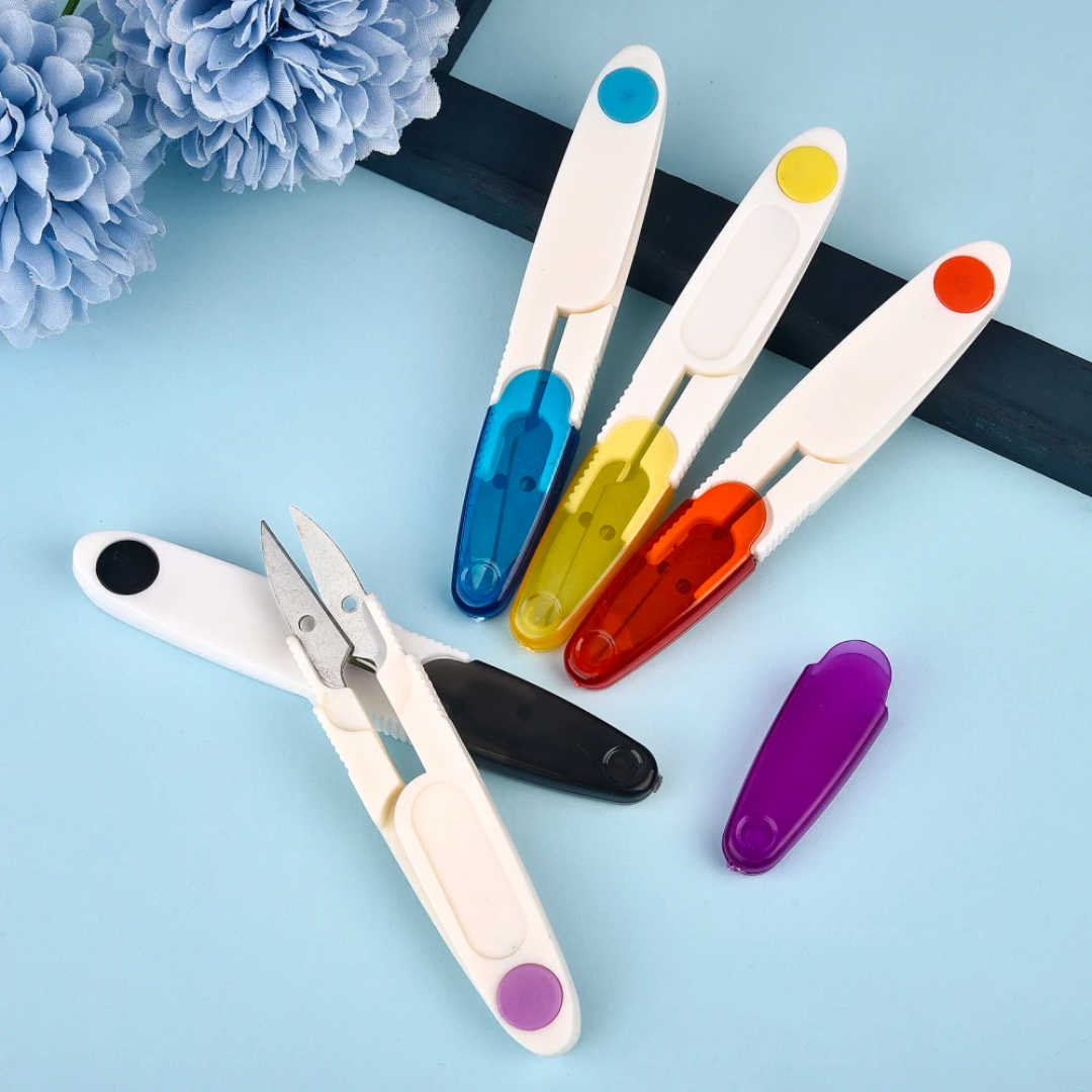 Assorted colors of Yarn Thread Snips with plastic handles and protective covers displayed on a blue background.