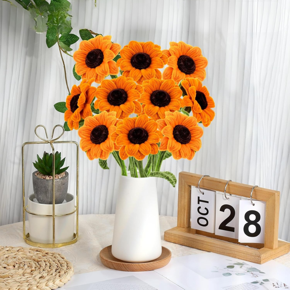 A Sunflower Crochet Kit vase sits on a table next to a potted plant and a wooden calendar showing October 28.