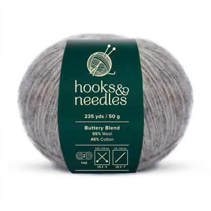 A ball of "hooks & needles" Buttery Blend Yarn 50g, offering 235 yards of fine-weight yarn comprised of a luxurious blend of 55% wool and 45% cotton. The label conveniently provides information on needle sizes and yarn thickness.