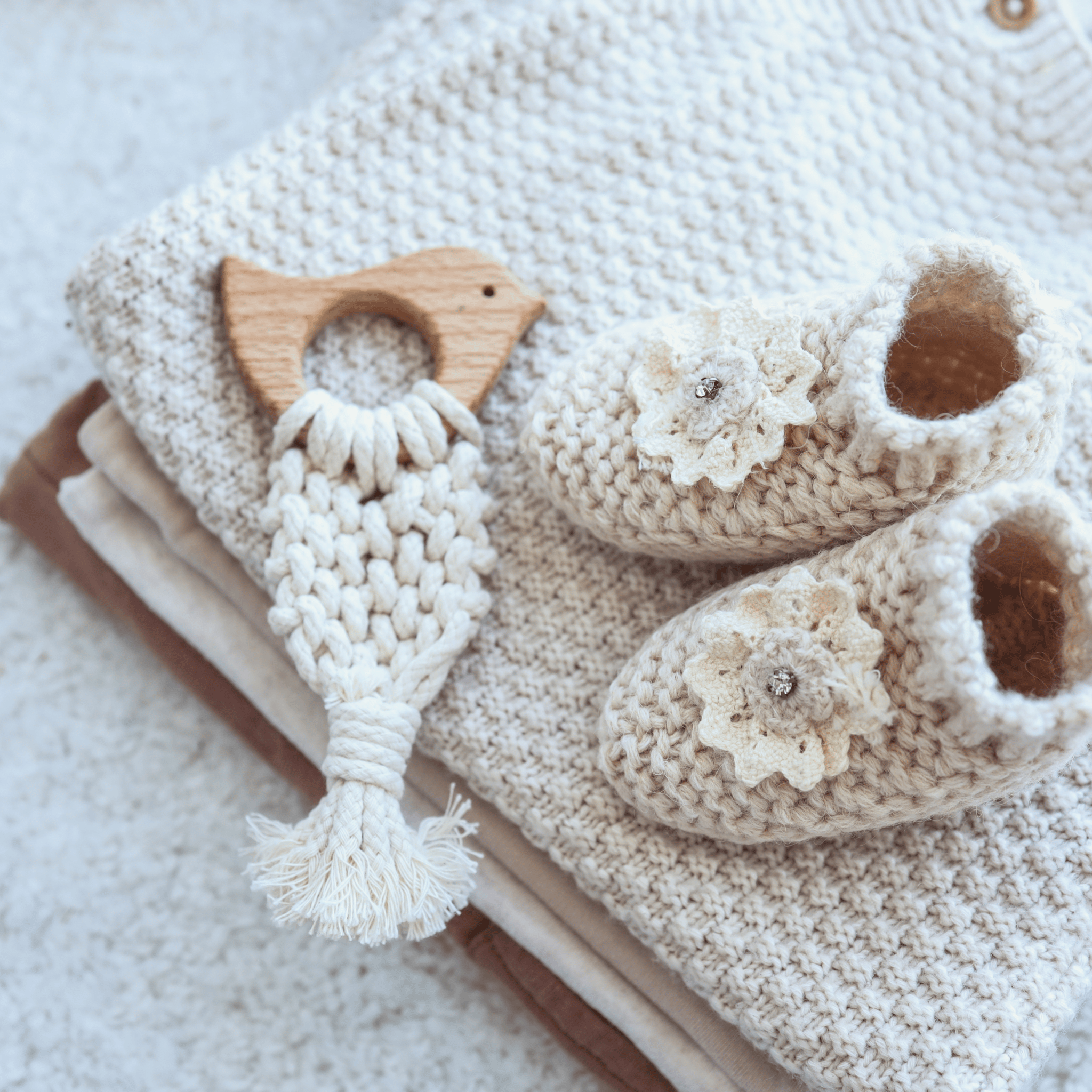 Hand-knit baby booties with floral decorations placed next to a [6-Month-Prepaid] Hooks & Needles Subscription Box #26 and a stack of knitted blankets on a light surface.