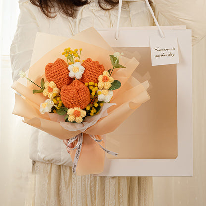 A person holds a bouquet of white and orange crochet flowers, named "Crochet Tulip Bouquet: Springtime in Every Stitch," wrapped in paper. It is accompanied by a gift bag reading "Tomorrow is another day." This handcrafted floral arrangement embodies timeless beauty and hope.