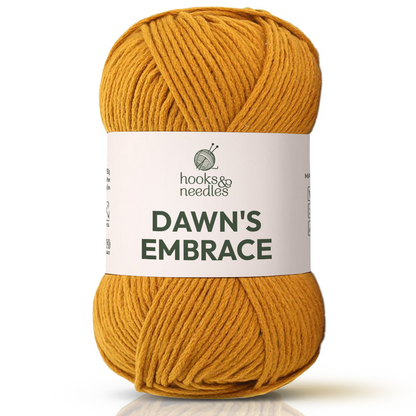 A skein of Dawn's Embrace Yarn in yellow, bulky weight, with a label showing knitting needles and yarn—ideal for crafting a cozy blanket.