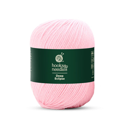 A light pink skein of Deep Eclipse Yarn 100g, featuring a dark green label that says "hooks & needles, Deep Eclipse." Made from 100% wool, this yarn is perfect for your crafting needs.